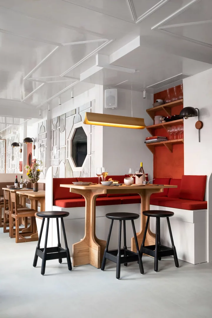 Grand Pigalle Experimental otelinin restoranı Frenchie Pigalle'dan, Dorothée Meilichzon imzalı iç mekân tasarımıyla dikkat çeken, modern ahşap masalar, kırmızı minderli beyaz banklar, siyah tabureler, turuncu duvar ve raflarda sıralanmış şarap kadehleri ile samimi bir akşam yemeği atmosferi sunan bir kare.