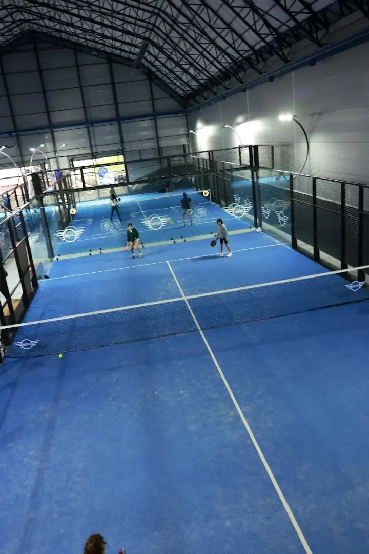 Beşiktaş, İstanbul'daki modern bir kapalı tesiste, mavi zemine sahip, fileli ve cam duvarlarla çevrili geniş bir padel kortunda raketleriyle aktif olarak padel oynayan birkaç kişi, parlak ışıklar altında spor yaparken görülüyor.