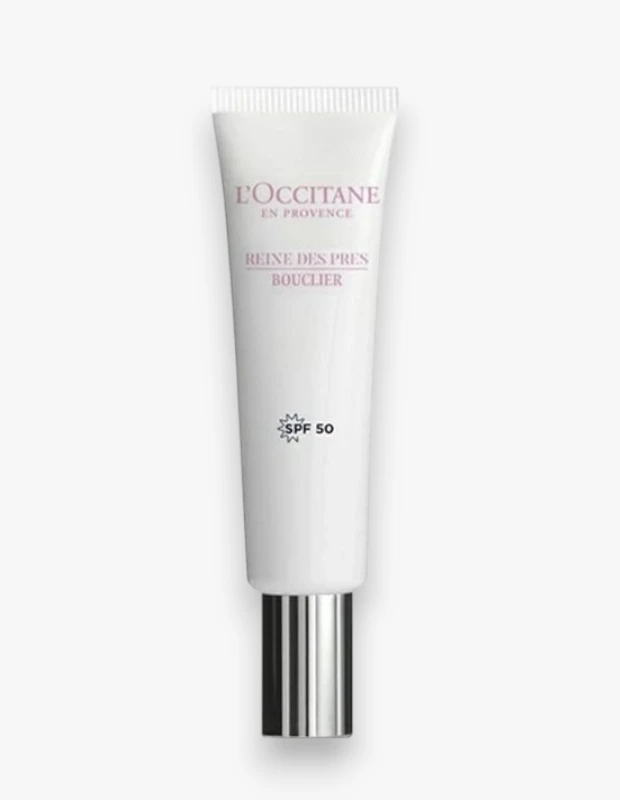 Beyaz bir zeminde dikey duran, alt kısmında parlak gümüş bir kapağı olan L'Occitane Reine des Prés markalı, SPF 50 güneş koruma faktörlü ve UV kalkanı özelliği sunan bu beyaz tüp, cilt koruması için önemli bir ürünü açıkça sergiliyor.