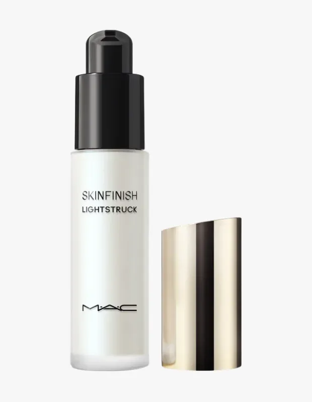 Beyaz, buzlu camdan yapılmış, siyah pompalı aplikatöre sahip, üzerinde belirgin bir şekilde SKINFINISH LIGHTSTRUCK ve MAC logosu bulunan cilt makyajı ürünü, hafif açılı, metalik altın rengi kapağıyla birlikte beyaz bir arka plan üzerinde zarifçe duruyor.