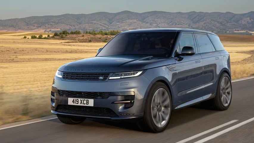 Koyu renkli, modern bir Range Rover Sport SUV, kuru otlaklar ve dağlık bir arka plan önünde asfalt yolda ilerlerken, mild-hybrid araçların gelecekteki çevresel faydalarını ve verimliliğini vurguluyor.