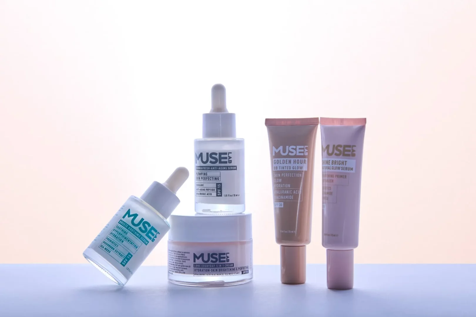 Açık renkli, yumuşak pembe-beyaz bir zeminde, Muse Lab markasına ait, üzerinde SPF korumalı yaşlanma karşıtı serum, nemlendirici krem, leke giderici ve aydınlatıcı serumlar, BB renkli nemlendirici ve makyaj bazı gibi çeşitli cilt bakımı ürünleri estetik bir düzende sergileniyor.