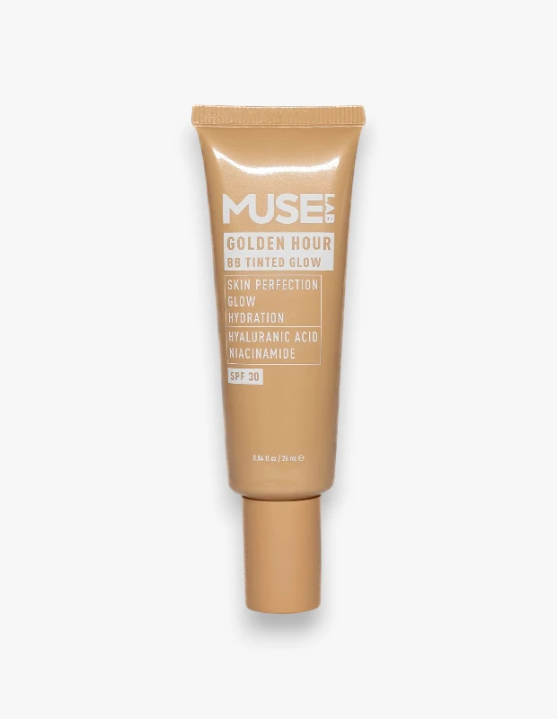 Beyaz bir arka plan üzerinde dikey olarak konumlandırılmış, altın rengi tonlarında, üzerinde MUSE GOLDEN HOUR BB TINTED GLOW yazılı, cilt mükemmelliği, ışıltı ve nemlendirme özelliklerine sahip, SPF 30 korumalı, hyaluronik asit ve niasinamid içeren bir BB kremi tüpü.