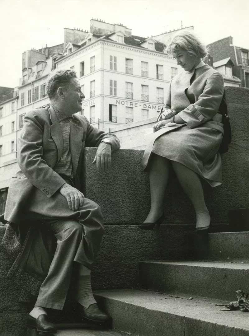 1961 yılında Nazım Hikmet ve Vera Tulyakova'nın Paris'te, Hotel Notre-Dame'ın göründüğü bir taş duvarda yan yana otururken çekilmiş, sakin bir sohbet anını yansıtan siyah beyaz fotoğraf.