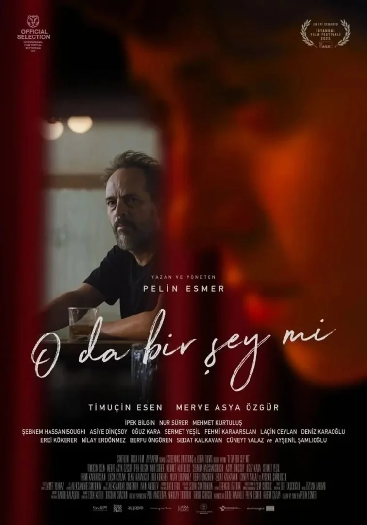 Kırmızı ve sıcak tonların hakim olduğu, yer yer bulanık ön plandan bakarken ciddi ifadesiyle dikkat çeken sakallı bir adamın önünde bardağıyla oturduğu O da bir şey mi adlı film afişi, üst kısımda Uluslararası Rotterdam ve İstanbul Film Festivalleri seçkilerinde yer aldığını gösteren ödül logoları barındırıyor.