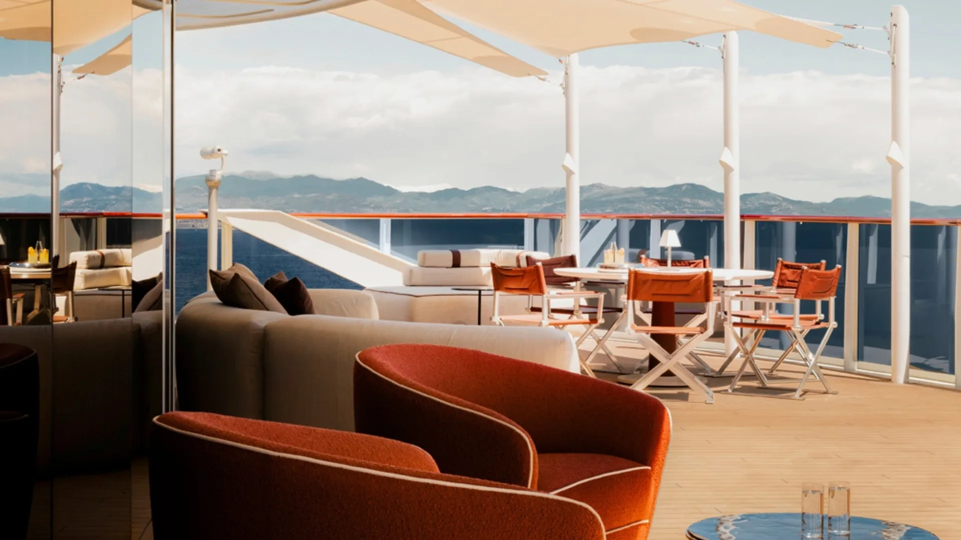 Geniş bir lüks cruise yatının güvertesindeki bu ferah yaşam alanında, rahat turuncu koltuklar ve şık bir masa takımıyla çevrili gölgeli dinlenme alanı, deniz manzarası eşliğinde mahremiyet ve üst düzey yat konforu sunuyor.