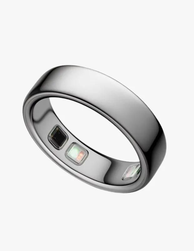 Beyaz bir arka plan üzerinde hafifçe eğik duran, gümüş rengi ve minimalist tasarımlı bir Oura Ring, iç kısmındaki sensörleri belirgin bir şekilde göstererek bu ekransız akıllı wellness yüzüğünün veri toplama özelliğini vurguluyor.