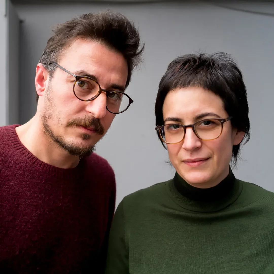 Friz ve heykel çalışmalarıyla tanınan sanatçılar Özlem Günyol ve Mustafa Kunt, gri bir duvar önünde, kısa saçlı Günyol koyu yeşil boğazlı kazakla ve sakallı Kunt bordo kazakla, ikisinin de gözlükleriyle doğrudan kameraya baktığı bir yakın çekimde poz veriyor.