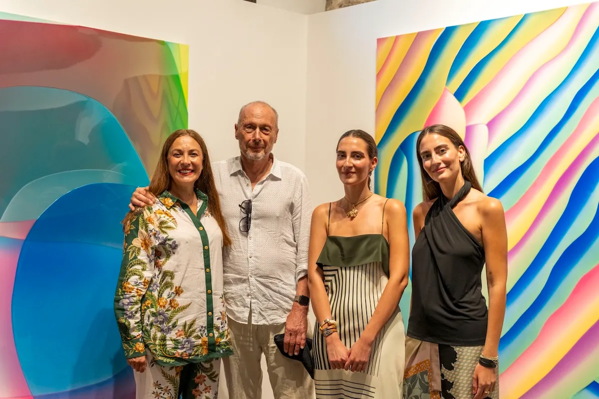 Sanat galerisinde Özlem Gusar, sanatçı Peter Zimmermann, Lal Ösen ve Selmin Ösen'in gülümseyerek poz verdiği bir an; arkalarında canlı renklerde, girdaplı ve dalgalı şeritler içeren iki soyut sanat eseri dikkat çekiyor.