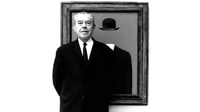 Belçikalı sürrealist ressam René Magritte, takım elbisesi ve kravatıyla ciddi bir ifadeyle izleyiciye bakarken, arkasındaki ahşap çerçeveli tablosunda tipik melon şapkalı ve başı gizlenmiş bir figürün betimlendiği kendi ikonik eserlerinden biriyle poz veriyor.