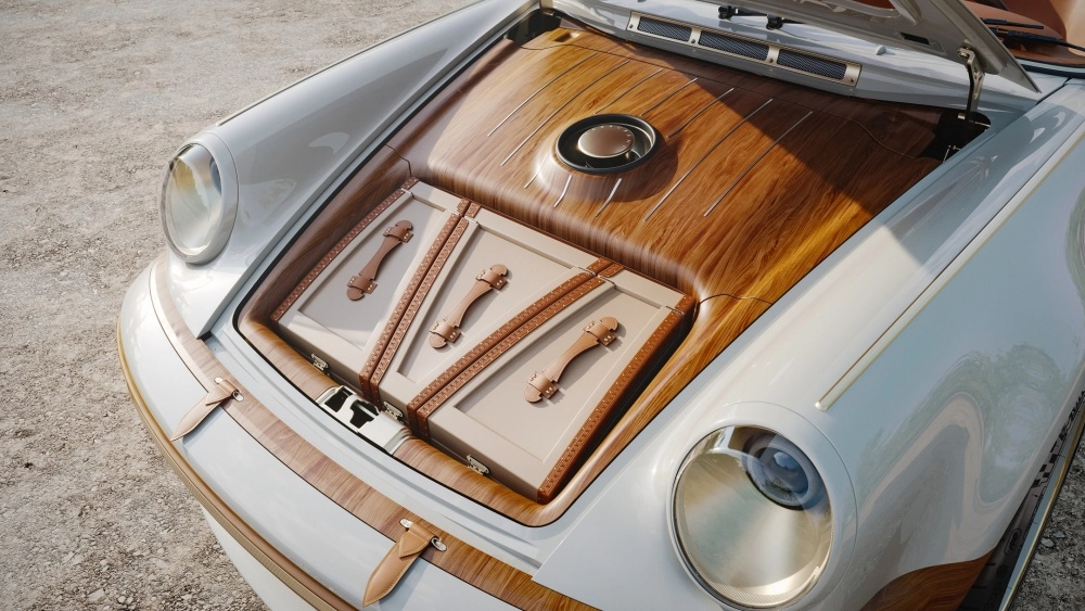 Beyaz, restomod bir Porsche 911'in ahşap detaylarla bezeli açık ön bagajında, Louis Vuitton iş birliği ruhunu yansıtan, bej renkli özel tasarım valizler kahverengi deri kayışlarla şıkça sabitlenmiş.