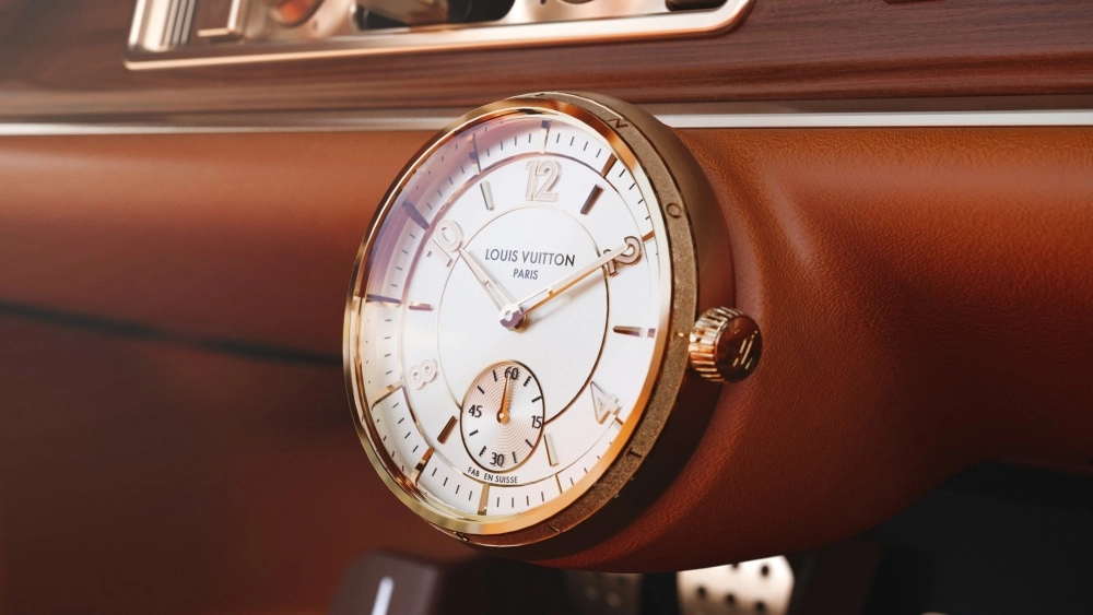 Singer Porsche 911 restomod aracının kahverengi deri ve ahşap kaplamalı gösterge panelinde konumlandırılmış, Louis Vuitton markalı, beyaz kadranlı ve altın rengi detaylara sahip lüks Tambour kokpit saati yakın çekimde gösteriliyor.