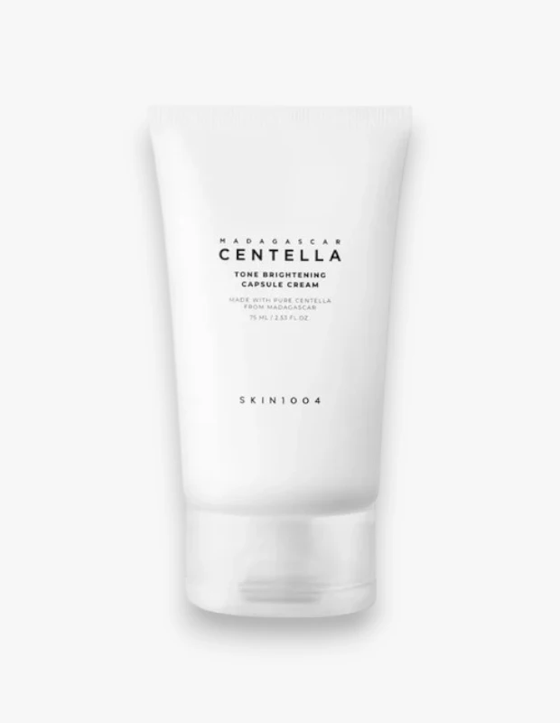 Düz beyaz bir zeminde hafifçe açılı duran, beyaz renkteki SKIN1004 Madagascar Centella Tone Brightening Capsule Cream'in 75 ml'lik tüpü, üzerinde Madagaskar'dan saf sentella ile yapıldığı belirtilen yazılarla cilt tonunu eşitlemeyi ve aydınlatmayı hedefleyen bir ürün olarak görünüyor.