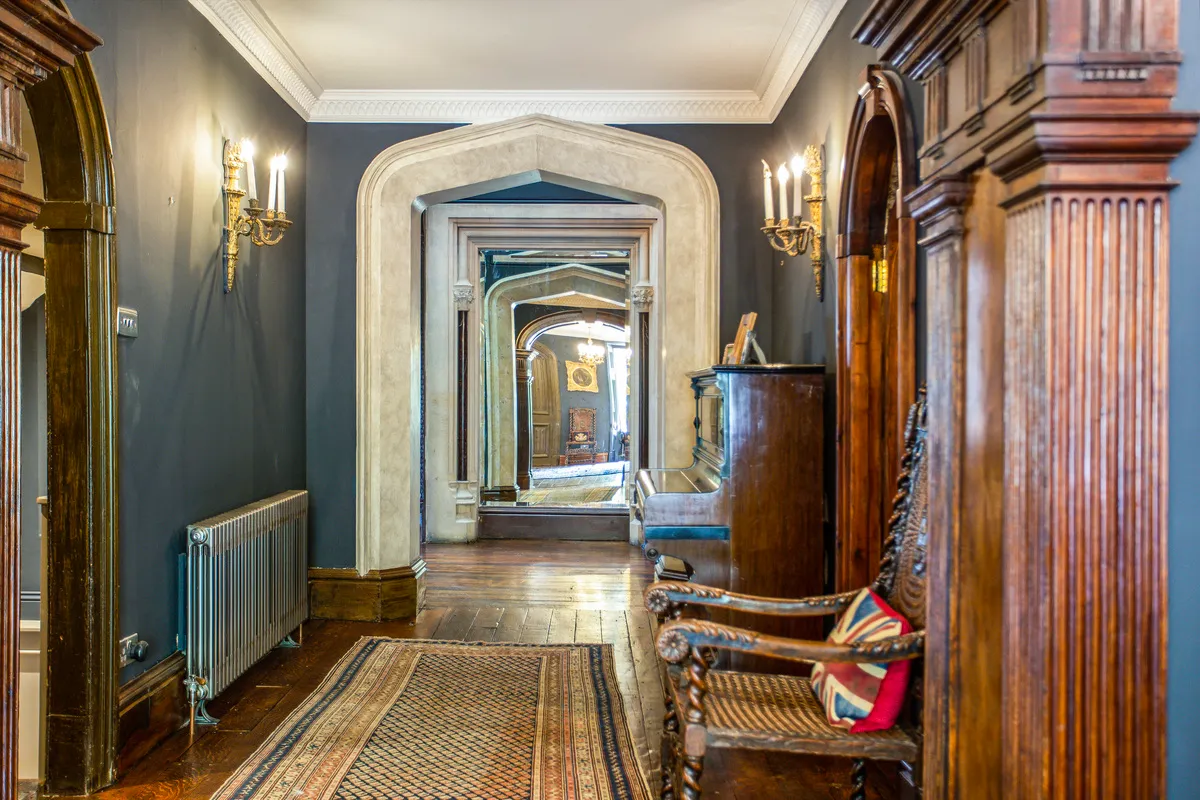 Stanley Park'ta yürütülen restorasyon çalışmaları kapsamında yenilenen, koyu gri duvarlı, ahşap parke zeminli, oyma motifli antika mobilyalar ve modern bir radyatörün bir arada bulunduğu, derinlik hissi veren kemerli bir koridor.