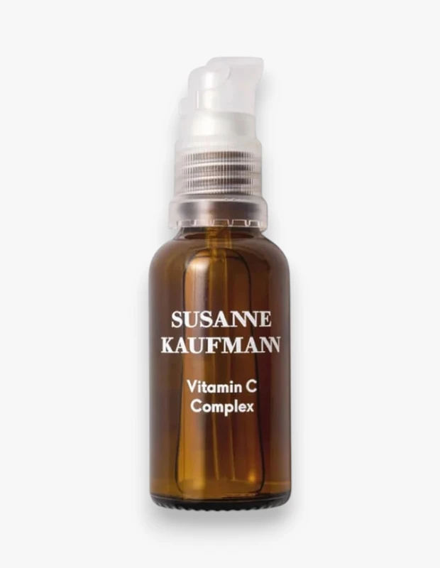 Beyaz bir arka plan üzerinde duran, üzerinde SUSANNE KAUFMANN Vitamin C Complex yazan kahverengi cam bir şişe ve şeffaf pompalı aplikatörü, C Vitamini kompleksinin içeriğini vurgulayan doğal bir görünüm sunuyor.