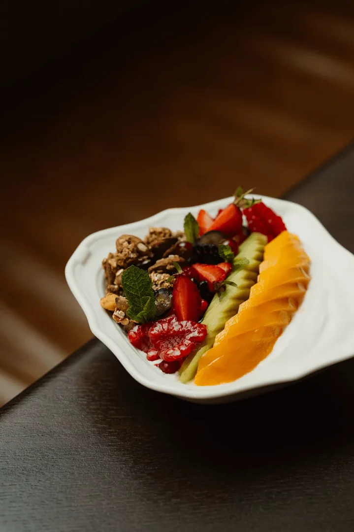 Beyaz, dalgalı kenarlı bir tabakta sunulan, taze çilek, frambuaz, yaban mersini, dilimlenmiş kivi ve mango ile zenginleştirilmiş, nane yaprağıyla süslenmiş granolalı veya müsli karışımı içeren bu renkli ve sağlıklı kase, Temple & Chapon'un hafta sonu brunch menüsünün ferahlatıcı seçeneklerinden biri olarak göz alıcı duruyor.