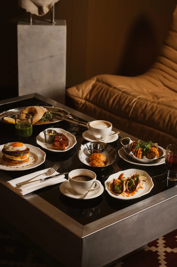 Koyu renkli parlak bir masada, kızarmış yumurtalı yiyecekler, mini tacolar, hamur işleri, bagel ve çeşitli lezzetlerle dolu tabaklarla birlikte kahve ve içeceklerin sunulduğu Temple & Chapon'un zengin brunch menüsü, New York chophouse kültürünü Fransız mutfağıyla buluşturan konsepti yansıtıyor.