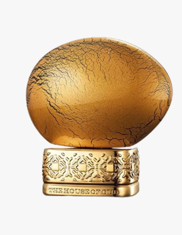 The House of Oud Golden Powder parfüm şişesi, üst kısmı çatlaklar ve pürüzlü dokusuyla altın tozunu andıran oval bir kapakla ve altında markanın adının oyulmuş olduğu desenli altın renkli dikdörtgen bir tabanla beyaz bir arka planda sergileniyor.