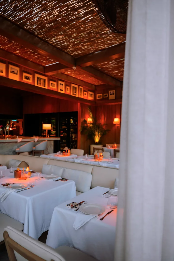 Bir trattoria içindeki samimi atmosfer, beyaz masa örtülü masalar, her masada sıcak bir ışık yayan lambalar, ahşap panelli duvarlarda sıralanmış çerçeveli resimler ve bambu detaylı tavanla rahat ve davetkar bir yemek deneyimi sunuyor.