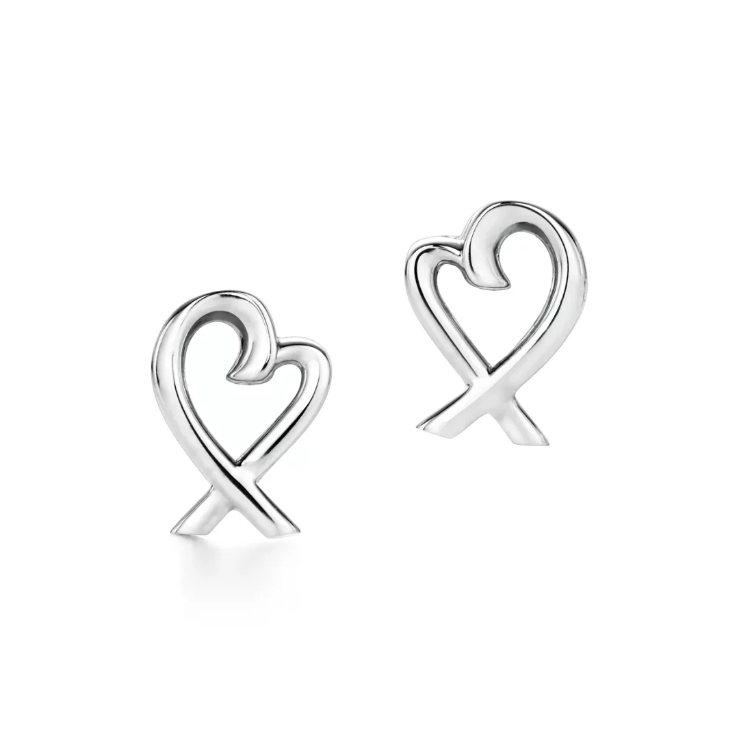 Beyaz bir zeminde sergilenen, parlak gümüş rengi iki adet Tiffany Picasso Loving Heart küpe, alt kısmında zarifçe çaprazlanan tek bir şeritten oluşan soyut kalp formunda tasarımıyla dikkat çekiyor.