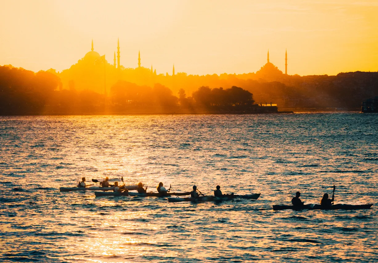Gün batımının turuncu tonlarıyla aydınlanan İstanbul silüeti önünde, ışıl ışıl denizde kürek çeken çok sayıda kişinin kayıklarla ilerlediği büyüleyici bir an, Türkiye'de kürek sporunun sunduğu eşsiz deneyimi vurguluyor.
