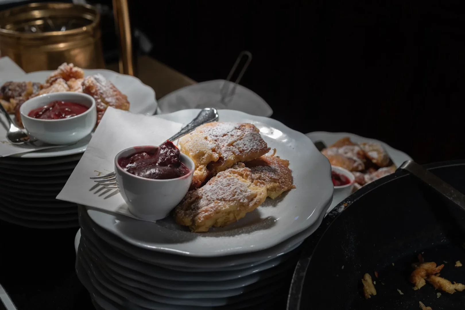 Beyaz tabaklarda sunulan, pudra şekeriyle kaplı, Viyana mutfağının meşhur lezzetlerinden biri olan parçalanmış pankekler (Kaiserschmarrn) ve yanında servis edilen koyu kırmızı meyve sosları, loş ışıklı bir büfede bolca bekliyor.