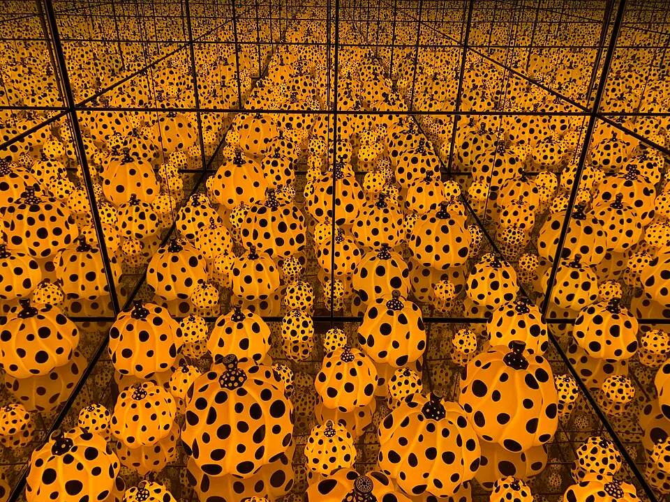Yayoi Kusama'nın balkabağı eserlerinden ilham alan bu görselde, aynalarla çevrili bir odada içten parlayan sarı ve siyah puantiyeli sayısız balkabağı, sonsuz bir derinlik ve tekrar hissiyle izleyiciyi büyüleyici bir deneyime davet ediyor.