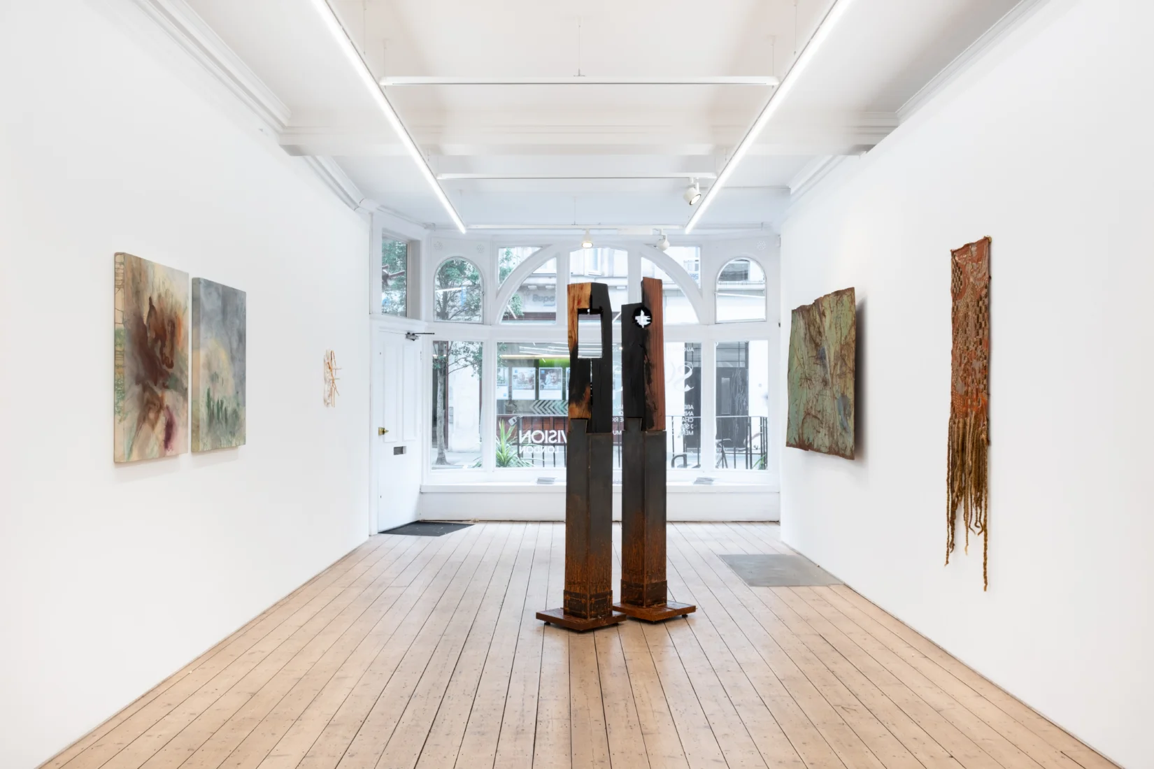 Vision Art Platform'da Charles-Joseph de Ligne'in Lightscapes sergisinden büyük, dikey bir fotoğraf eseri; parlak yüzeyi, mekânın ışığını ve izleyicinin siluetini görüntünün içine alarak, ışığın gösterdiği ve sakladığı arasındaki algı değişkenliğini vurguluyor.