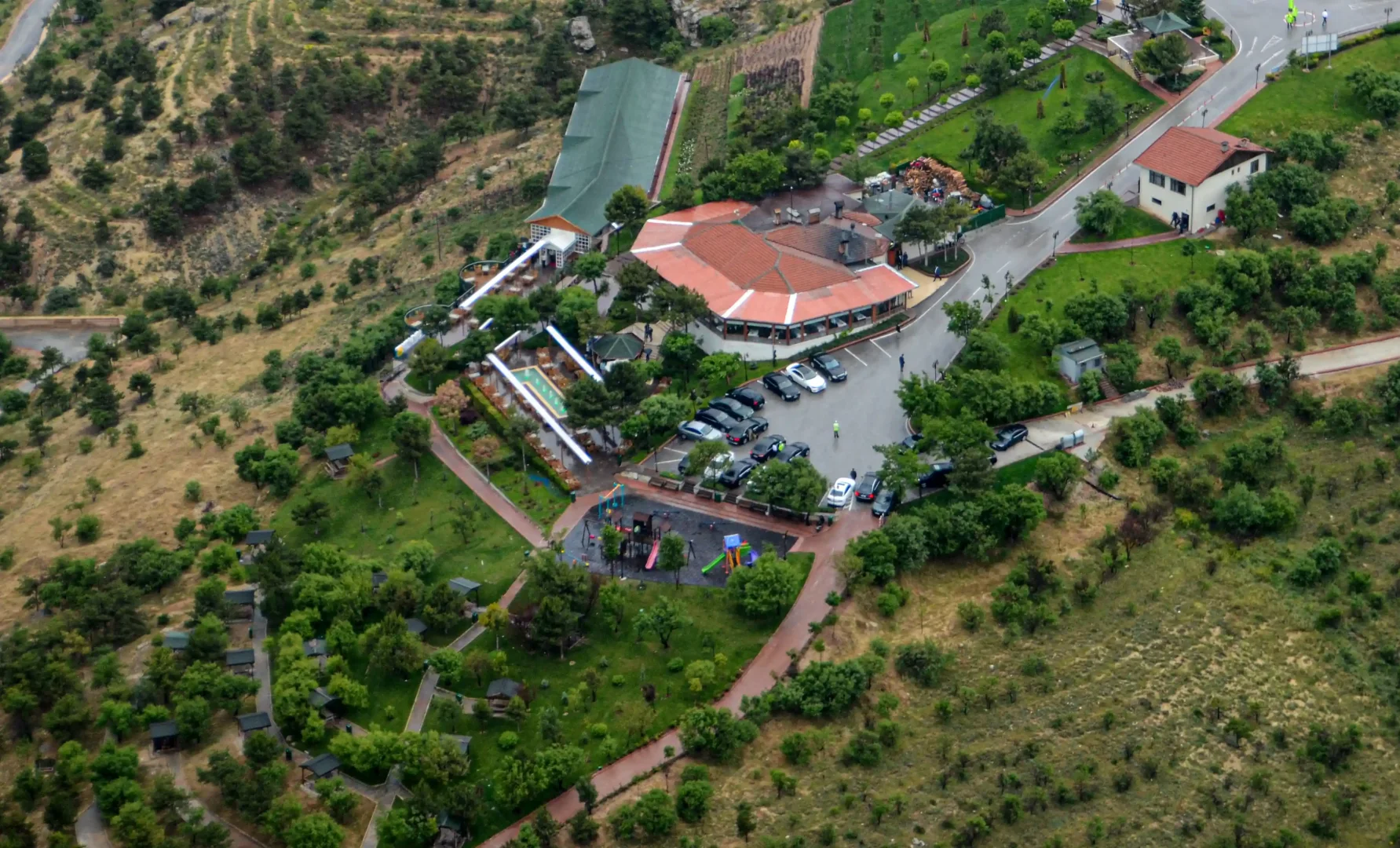 Akyokuş Parkı'nın havadan çekilmiş bu geniş görüntüsünde, kırmızı kiremit çatılı restoran binası, otoparkı, yemyeşil ağaçlar ve çimenlik alanlarla çevrili çocuk oyun parkı, piknik yerleri ve yamaç boyunca uzanan tesisler yer almaktadır.