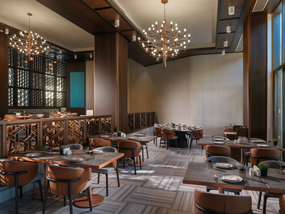 Anda Barut Collection bünyesindeki Kara A La Carte Restaurant'ın zarif iç mekanı, modern aydınlatmalı avizeler, geometrik desenli ahşap bölmeler ve konforlu kahverengi sandalyelerle donatılmış, geniş ve davetkar bir yemek alanı sunuyor.