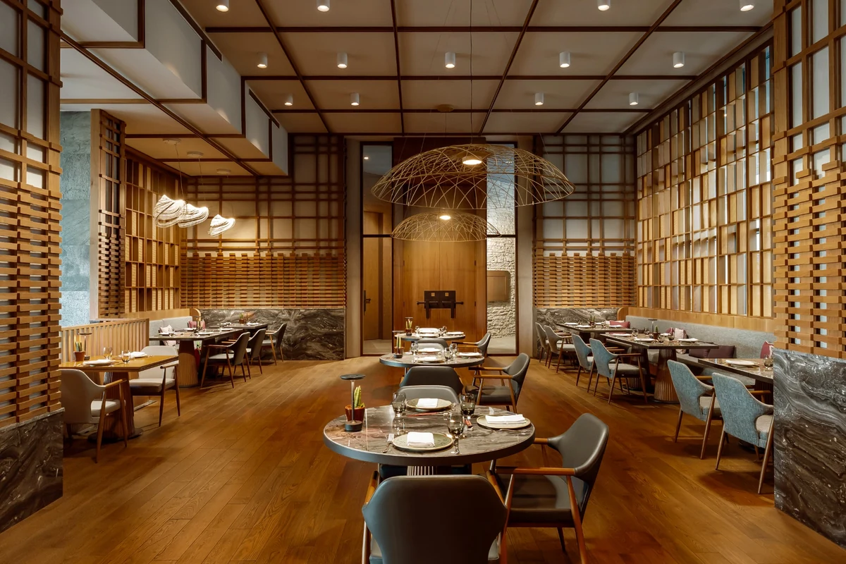 Anda Barut Collection Tiger Restaurant'ın sıcak ve modern iç mekanında, ahşap çıtalı duvarlar ve parke zeminle bütünleşen ambiyansta, dikkat çekici tel avizelerle aydınlatılmış, mermer yüzeyli masalar zarif sandalyelerle çevrili olarak misafirleri beklemektedir.