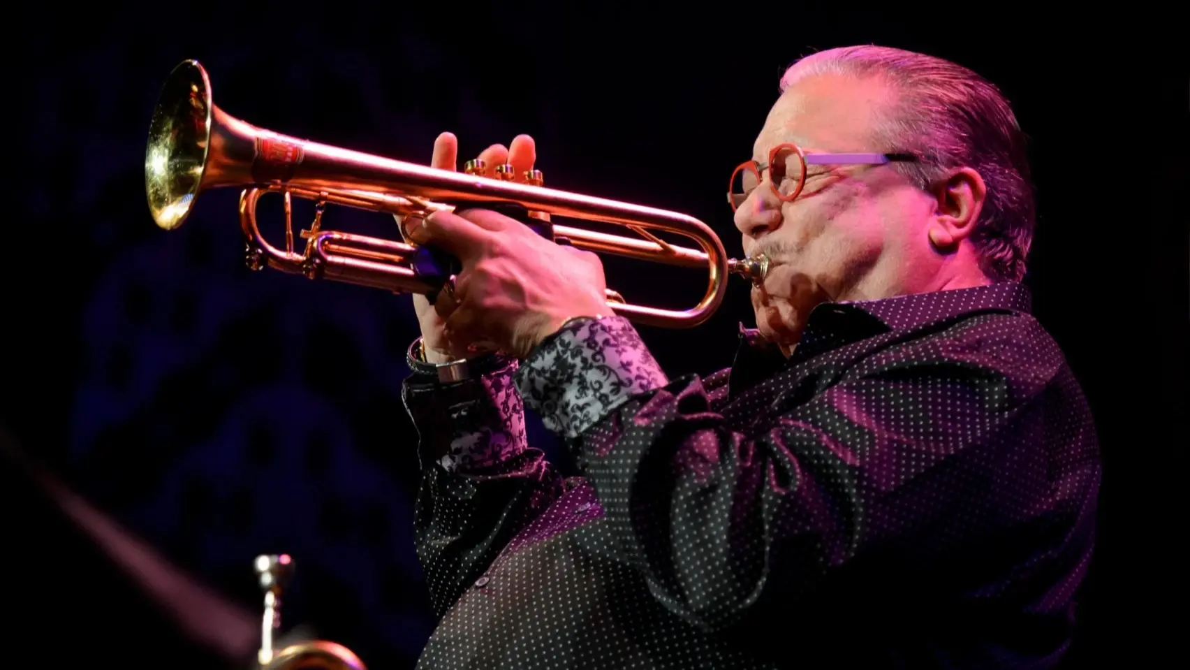 Akbank Caz Festivali sahnesinde trompetini tutkuyla çalan usta müzisyen Arturo Sandoval, spot ışıkları altında, müziğin ruhunu yansıtan dinamik bir pozla izleyicilere unutulmaz bir deneyim sunuyor.