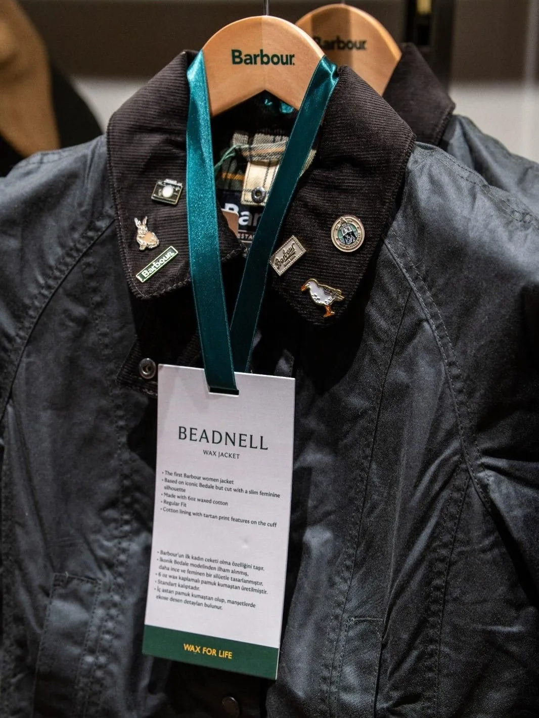 Barbour'un Tersane İstanbul'daki geniş ve aydınlık mağazasının iç görünümü, ahşap ve metal raf sistemlerinde sergilenen ikonik wax ceketleri, gömlekleri ve aksesuarlarıyla markanın İngiliz mirasını modern bir perakende ortamında sunarak, işlevselliği ve premium yaşam tarzını bir araya getiren koleksiyonları sergiliyor.