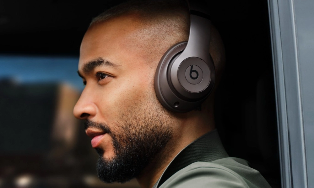 Kısa saçlı ve sakallı bir adamın yan profilden çekilmiş yakın planda görüntüsü, kulağında mat siyah renkli, belirgin b logosuna sahip Beats Studio Pro Wireless kulaklık ile müzik veya ses içeriğine dalmış haldeyken görülüyor. Bu kaliteli kablosuz kulaklık, kullanıcısına üstün bir dinleme deneyimi sunuyor gibi duruyor.