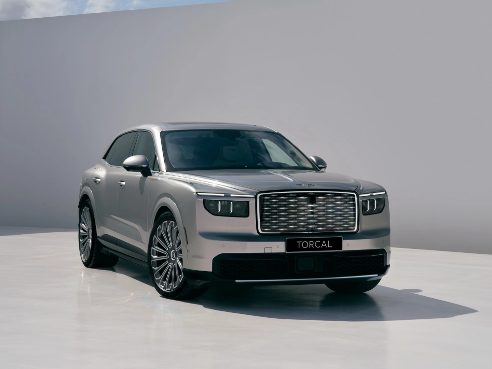 Karanlık ve parlak bir zeminde, fütüristik tasarım çizgilerine ve aerodinamik hatlara sahip, koyu renkli, güçlü duruşlu Bentley Torcal Elektrikli SUV modeli, yüksek performans potansiyelini vurgulayan modern farlarıyla dikkat çekiyor.