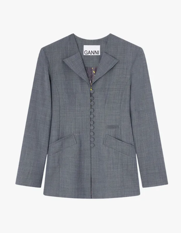 Beyaz bir arka plan üzerinde, GANNİ etiketli, V yaka ve sivri yakalı, önünde dikey bir düğme sırası ile iki kapaklı cebi bulunan, hafif dokulu gri blazer ceket, iç kısmında görünen renkli astar detayıyla ofis kombinleri için şık bir seçenek olarak sunuluyor.