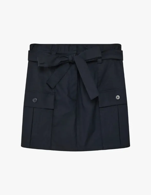 Koyu lacivert renkteki bu şık mini etek, beli kuşaklı ve önünde büyük fiyonk detayıyla dikkat çekerken, her iki yanında düğmeli kapaklı cepleri ve hafif piliseleriyle preppy tarzı başarılı bir şekilde yansıtıyor ve blazer kombinleri için mükemmel bir seçenek sunuyor.