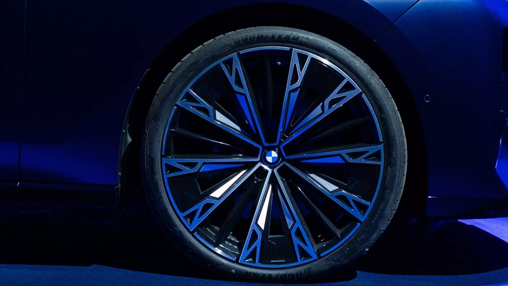 BMW 7 Serisi'nin arka koltuğundan görünen, lüks açık renk deri döşemeli iç mekanda, ön koltuk arkasına entegre edilmiş büyük ekranda canlı ve renkli bir Azusa Murakami ve Alexander Groves sanat eseri sergilenirken, alttaki dokunmatik kontrol paneli ve sağdaki dış mekan manzarası dikkat çekiyor.