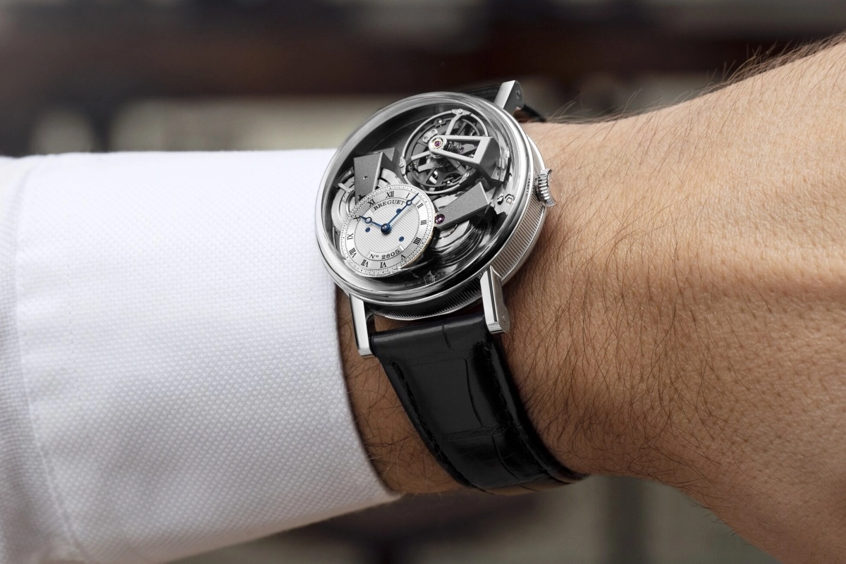Breguet Tradition Tourbillon 7047 saati, karmaşık tourbillon mekanizması ve detaylı iskelet yapısıyla altın tonlarında kasasının içindeki hassas dişli ve köprülerini gözler önüne sererek yüksek saatçilik zanaatini ve lüks tasarımını sergiliyor.