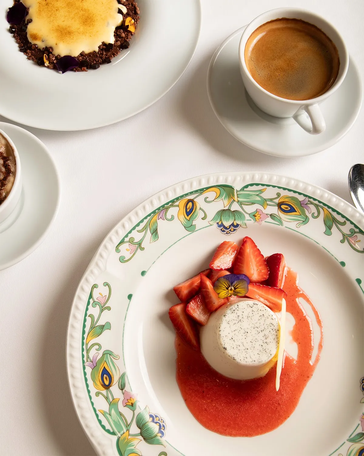 Da Mario restoranının yemyeşil ağaçların gölgelendirdiği açık hava terasında, beyaz masa örtülü yuvarlak ve dikdörtgen masalarda oturan çok sayıda misafir, garsonlar tarafından servis edilen lezzetlerin tadını çıkarırken sohbet ediyor ve samimi bir atmosferde keyifli bir yemek deneyimi yaşıyor.