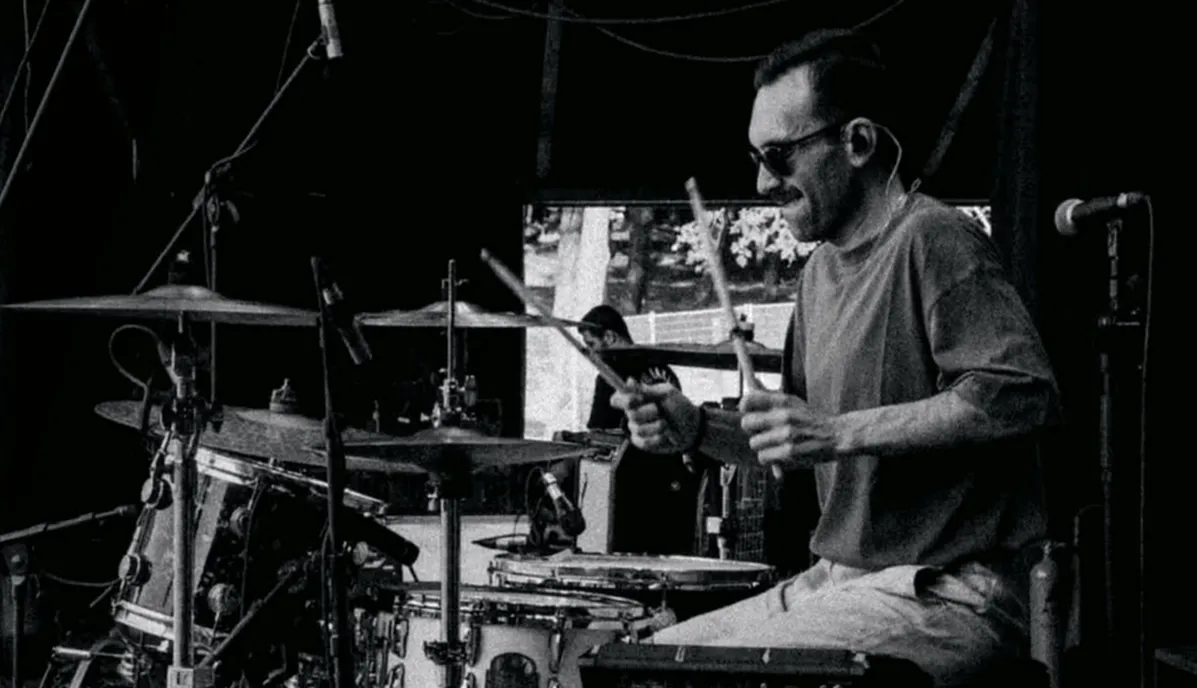 Fugamundi Caz Kulübü'nün sahnesinde bir davul seti, mikrofonlar ve diğer müzik aletlerinin yer aldığı, misafirlerin caz müziği dinlerken keyifli vakit geçirebilecekleri rahat ve şık oturma alanlarıyla donatılmış modern iç mekanı.