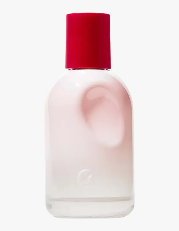 Glossier You parfüm şişesi, minimalist ve modern tasarımıyla öne çıkıyor; parlak kırmızı silindirik kapağı, içindeki pembe tonlarındaki zarif sıvıyı gösteren buzlu cam yuvarlak gövdesi ve alt kısmındaki kabartmalı marka detayıyla beyaz bir zeminde şık bir şekilde konumlanmış.