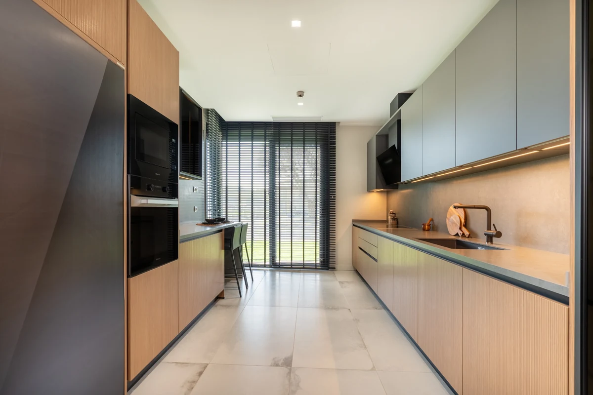 Doğal ışıkla aydınlanmış, ahşap tonlarında dolaplara, modern bir ocağa ve geniş bir pencereye sahip, minimalist ve ferah tasarımlı bu modern mutfak, şıklığı ve fonksiyonelliği bir araya getiriyor.