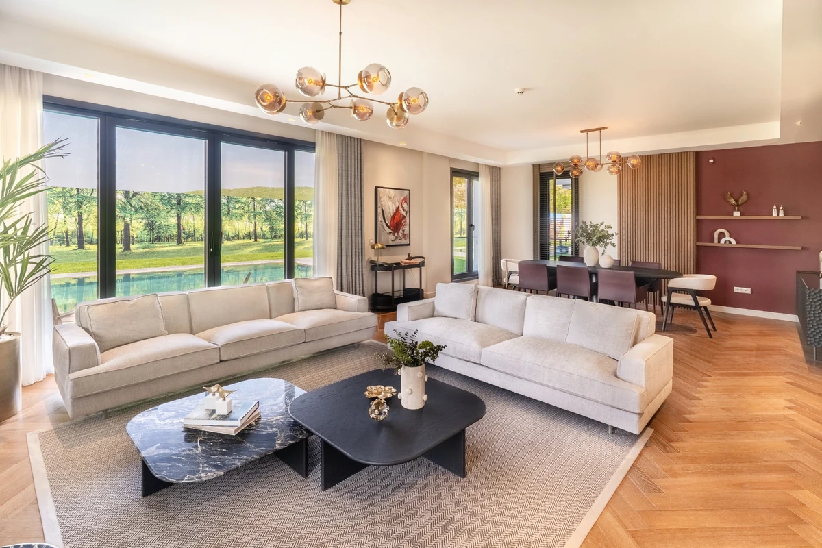 Şık ve minimalist çizgiler taşıyan, geniş pencerelerle dış mekanı içeri taşıyan bu modern salon, huzur veren bir yüzme havuzu ve kasaba atmosferi manzarası sunarak çağdaş yaşamın sakin bir deneyimini gözler önüne seriyor.