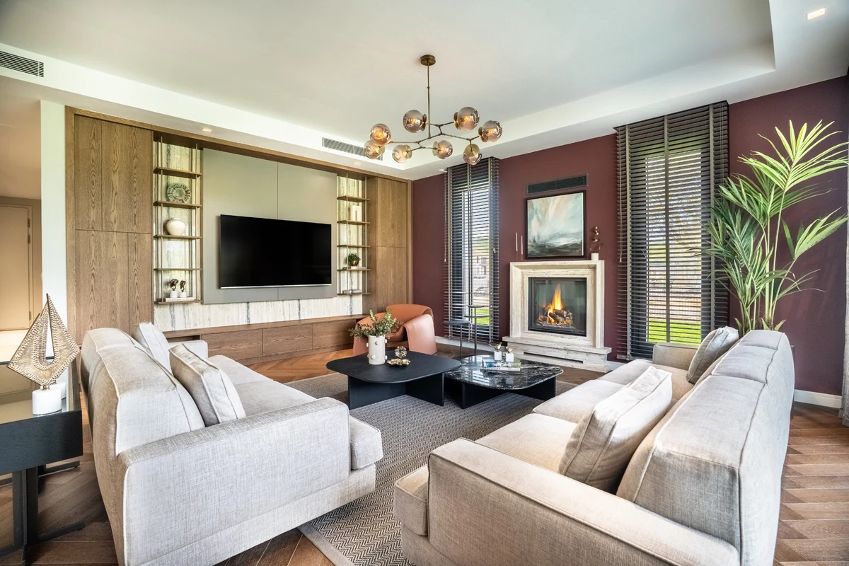 Bu geniş ve aydınlık modern salon, rahat krem rengi köşe koltuğu, şık orta sehpası ve dışarıyı gösteren büyük penceresiyle dikkat çekerken, özellikle minimalist tasarıma sahip duvardaki entegre şömine odanın sıcak ve davetkar atmosferini tamamlıyor.