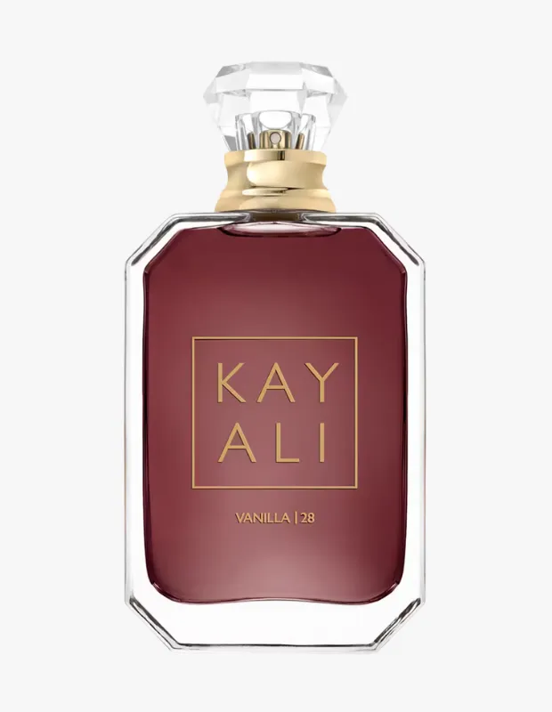 Bir Kayali Vanilla 28 parfüm şişesi, köşeleri zarifçe kesilmiş şeffaf cam gövdesi ve içindeki koyu bordo renkli sıvısıyla dikkat çekiyor; altın renkli çerçeve içinde Kayali yazısı ve altında küçük harflerle Vanilla | 28 ibaresi, elmas kesim şeffaf kapak ve altın renkli boyun kısmı ile sade açık gri arka plan üzerinde öne çıkıyor.