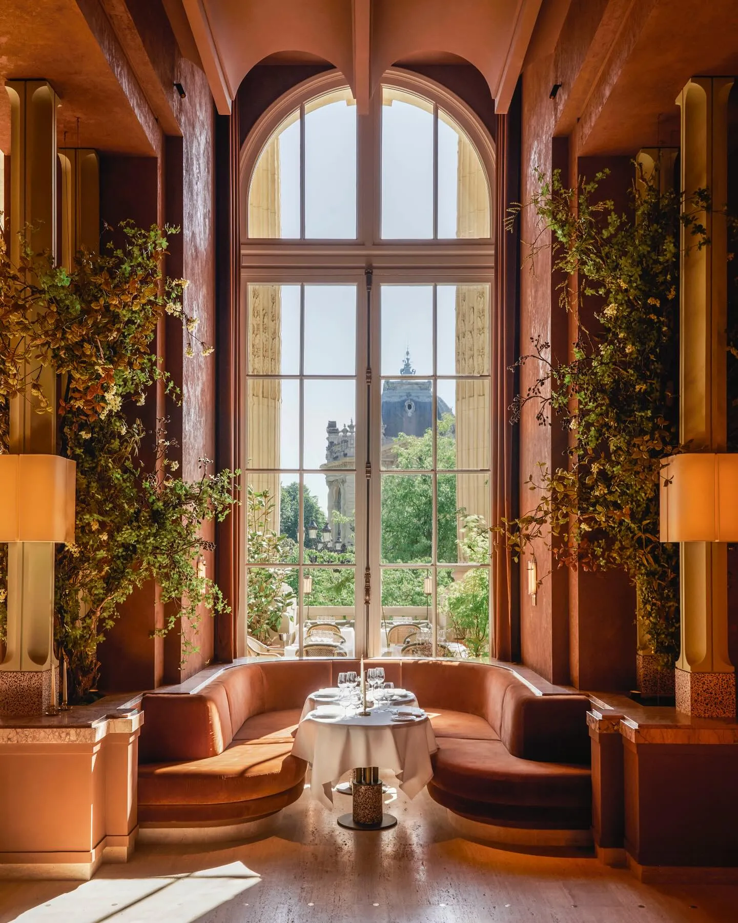 Paris'teki Le Grand Café'nin kemerli dev pencerelerinden dışarıdaki yemyeşil manzarayı içeri taşıyan, duvarları saran yeşilliklerle bezenmiş, toprak tonlarında şık ve görkemli iç mekanında, kadife banket oturma grubunun önünde zarifçe hazırlanmış yuvarlak bir masa yer alıyor.