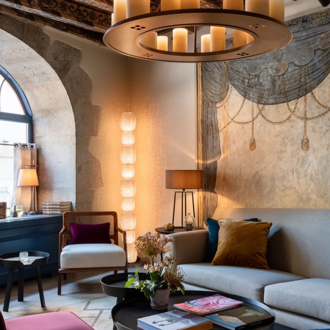 Les Armures Hotel'in lüks lobisi, taş kemerli penceresi, zarif mumlu avizesi ve duvar freskiyle geleneksel detayları modern mobilyalarla birleştiren bu otantik tasarım alanı, ziyaretçilerine sıcak ve davetkar bir atmosfer sunuyor.