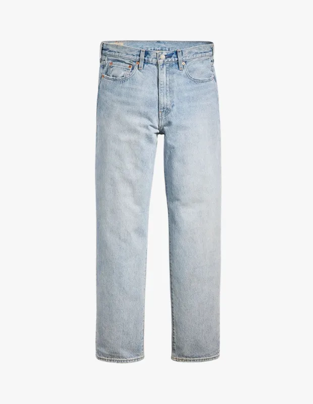Beyaz bir arka planda dikey duran, Levi's markasına ait, hafifçe yıpranmış görünümlü, açık buz mavisi tonlarında, rahat kesim bir kot pantolon, üst kısımda kemer halkaları ve ön cepler net bir şekilde görünmektedir.