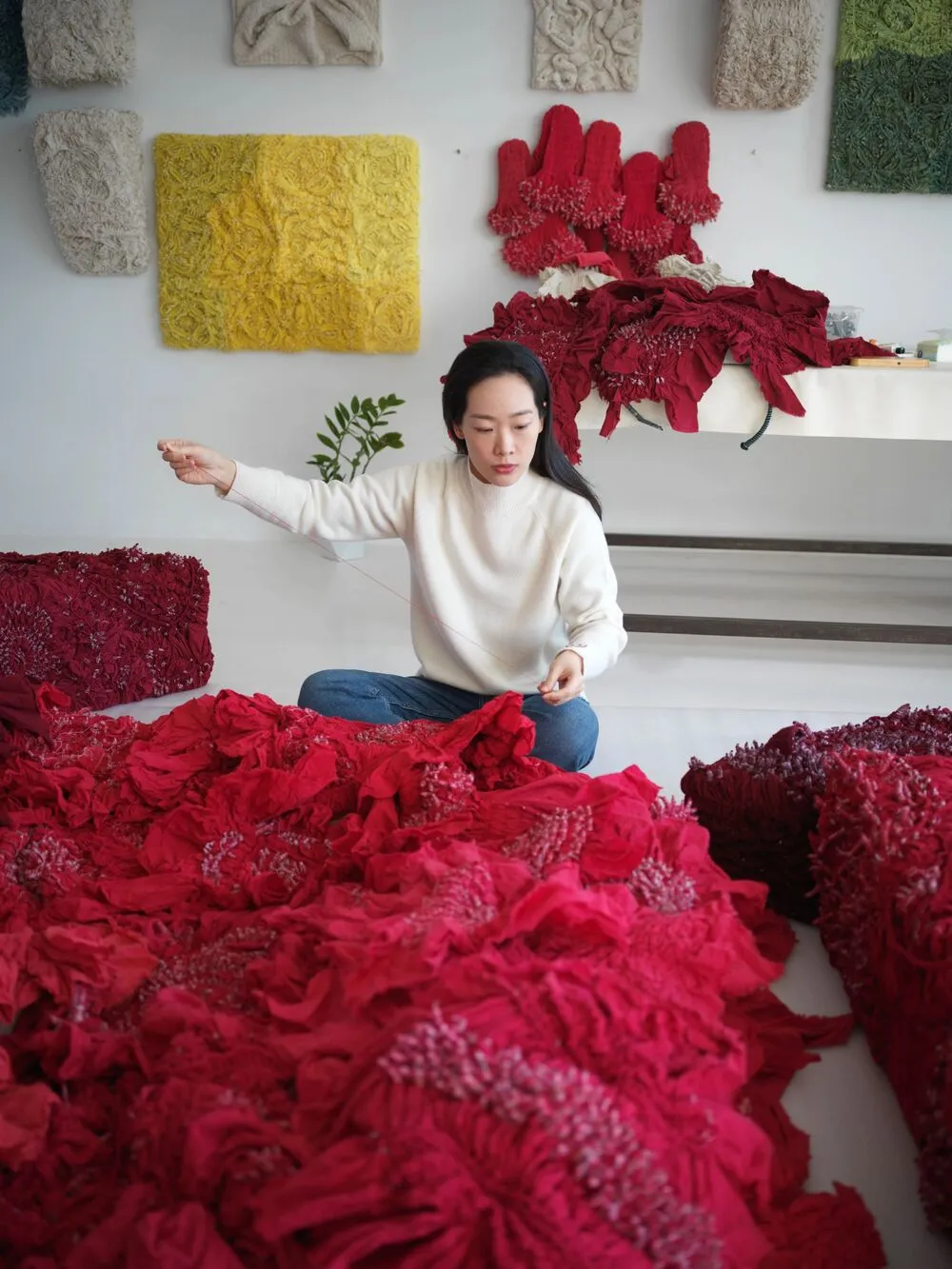 Lin Fanglu'nun geleneksel tekstil teknikleriyle oluşturduğu modern sanat enstalasyonunun bir detayı olan bu görselde, indigo mavisinin derin tonları, kumaşın katmanlı ve organik formları arasında ışık oyunları yaratarak izleyiciye dingin bir atmosfer sunarken, sanatçının el işçiliğine olan saygısı belirgin bir şekilde hissediliyor.